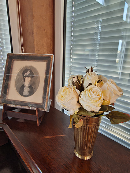 Ein Strauß weiße Rosen und ein altes gemaltes Portrait in Folie auf der Fensterbank