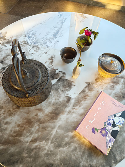 Schwarze Teekanne, Buch, Vase mit roter Rose und kleine Schalen auf Marmortisch